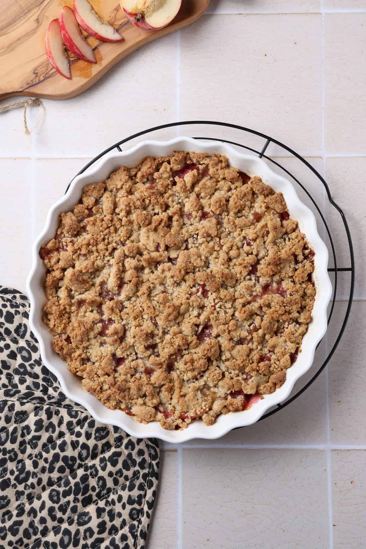 A peach crumble with hazelnut streusel in a round white baking dish.