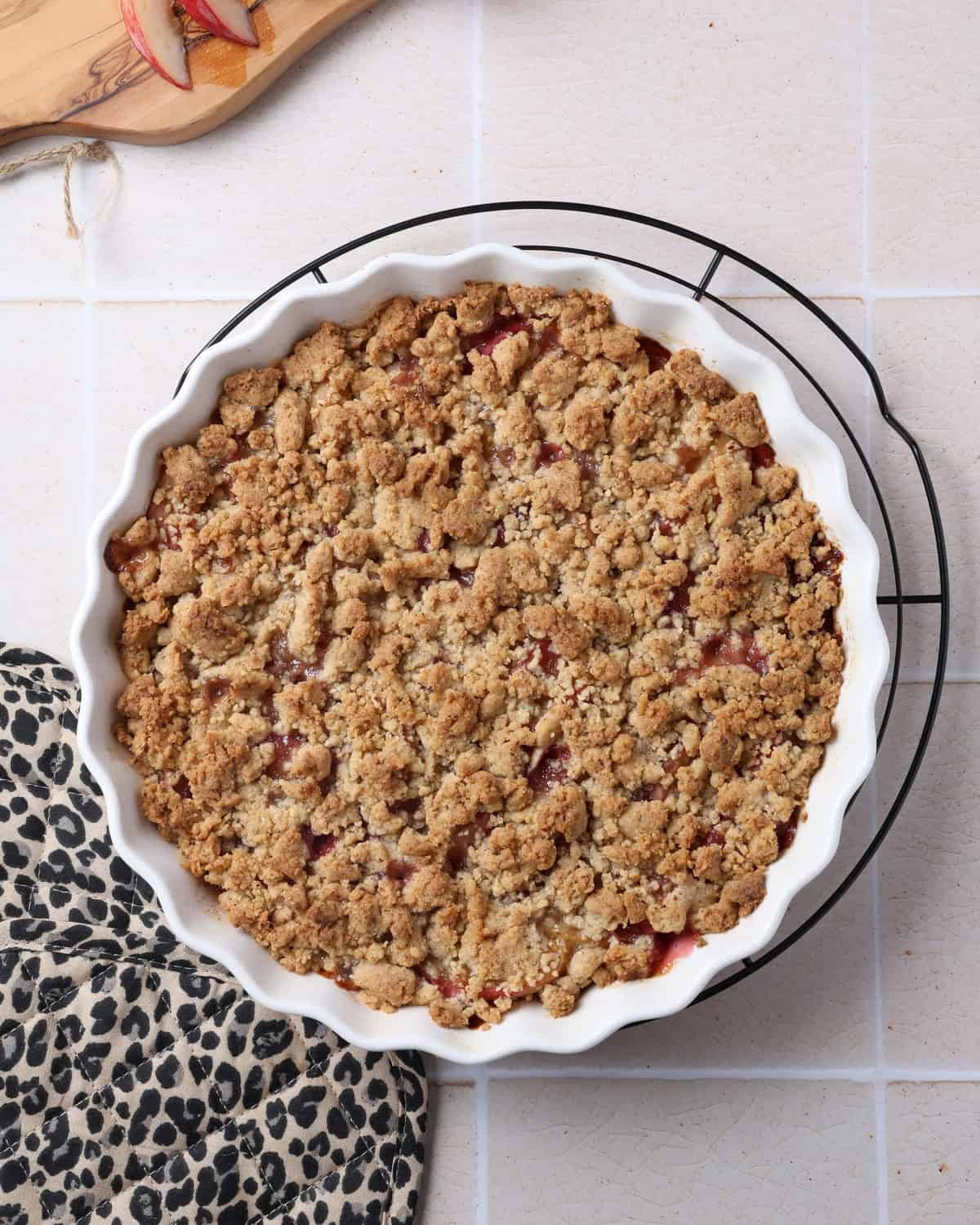 A peach crumble with hazelnut streusel in a round, white casserole dish.