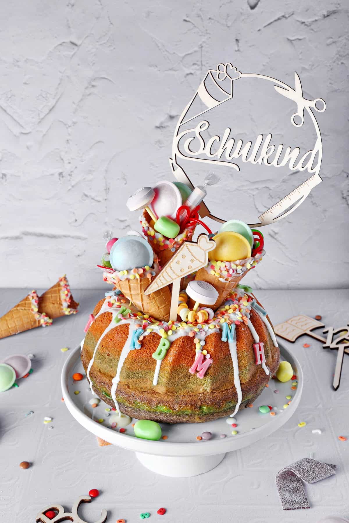 Colorful rainbow Bundt cake for the first day of school, decorated with chocolate glaze, filled ice cream cones, and a school kid cake topper.