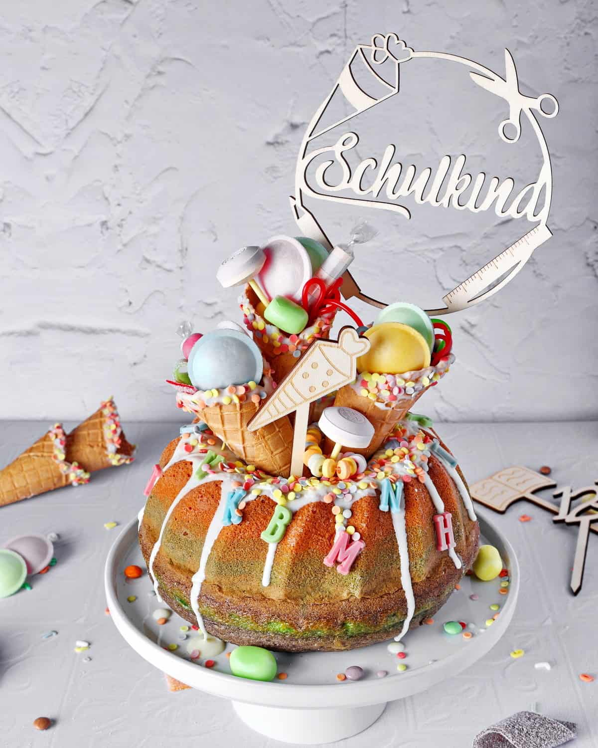 Colorful rainbow bundt cake for the first day of school, decorated with sweets in ice cream cones and a school child topper.