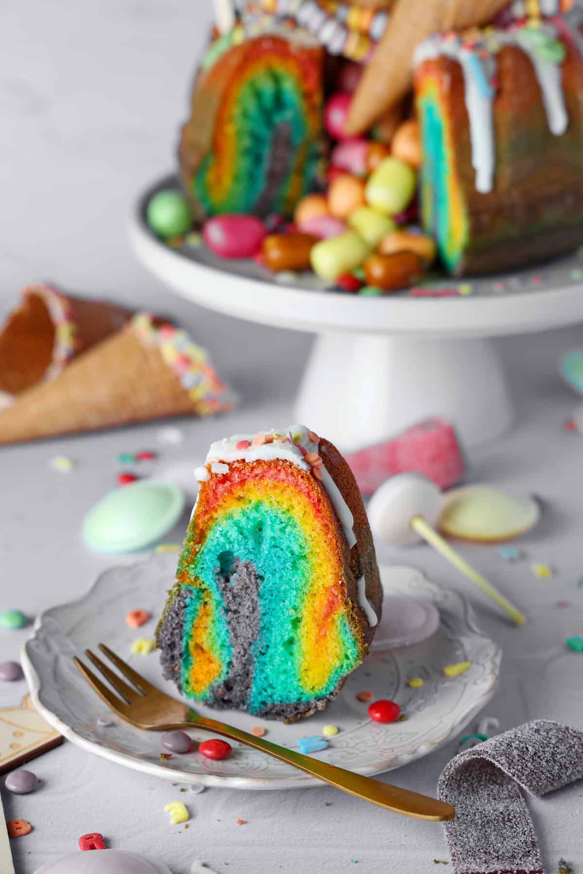 A slice of rainbow bundt cake on a plate with the sliced cake in the background.