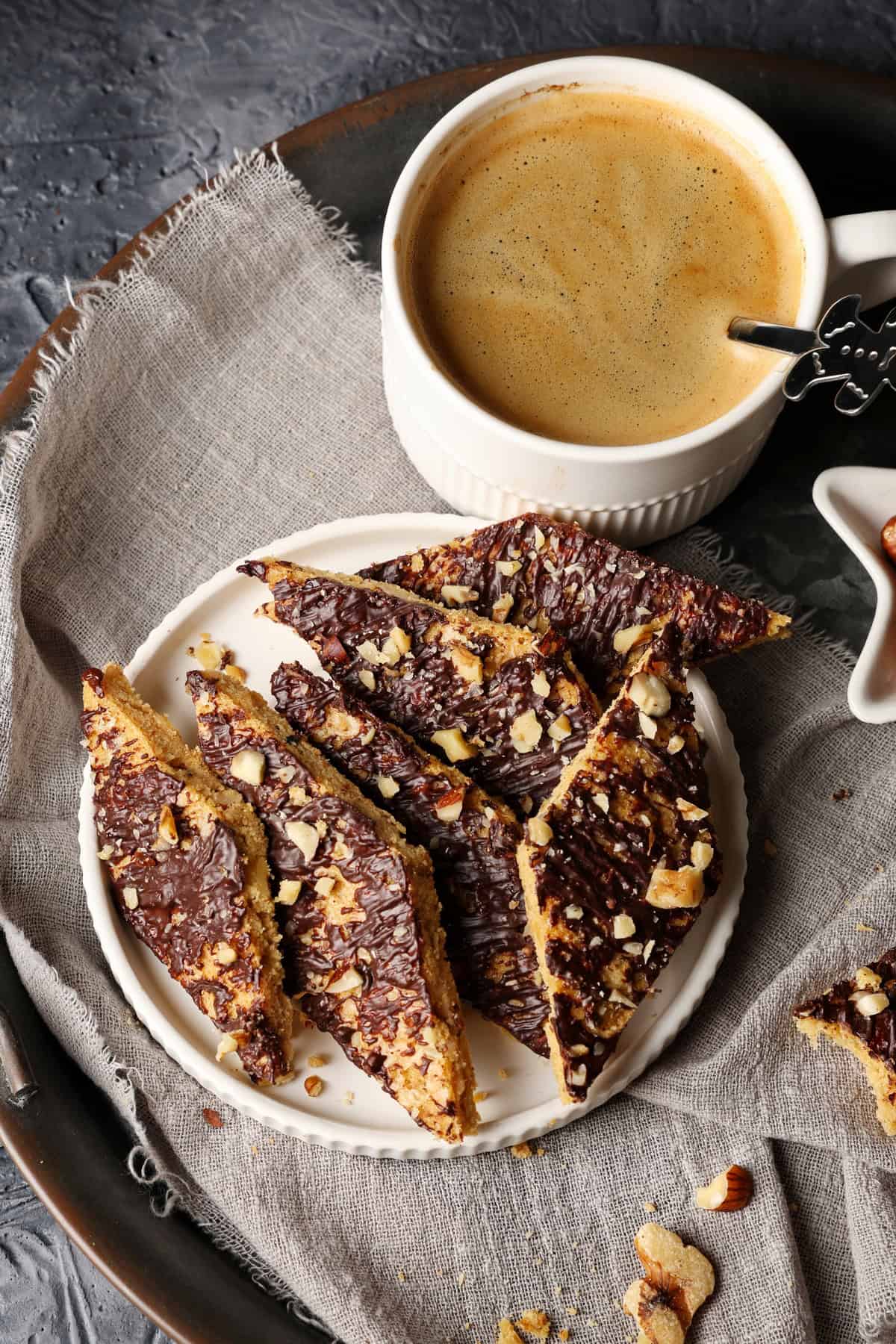 A small white plate with white chocolate speculoos bars, with a cup of coffee just above it.