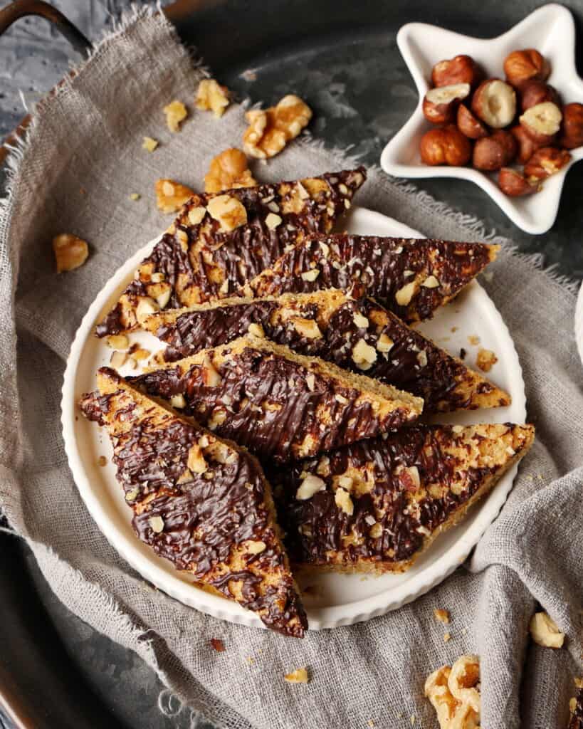 A plate of speculoos cookies with white chocolate. Above it, a small bowl with hazelnuts.