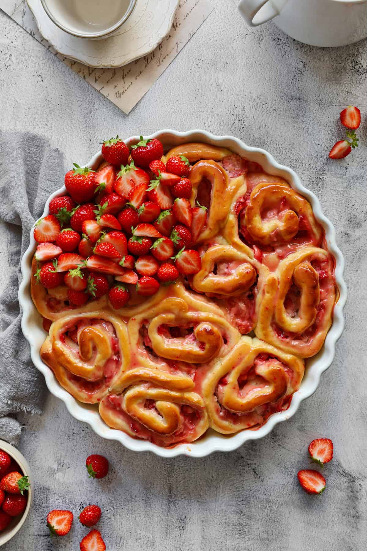 A round baking dish filled with strawberry rolls and fresh strawberries. Surrounded by extra strawberries for decoration.