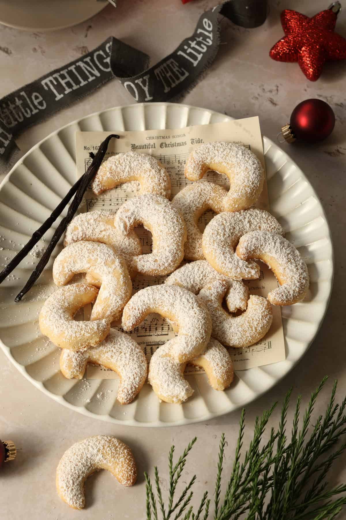 A white plate with vanilla crescent cookies and two vanilla beans.