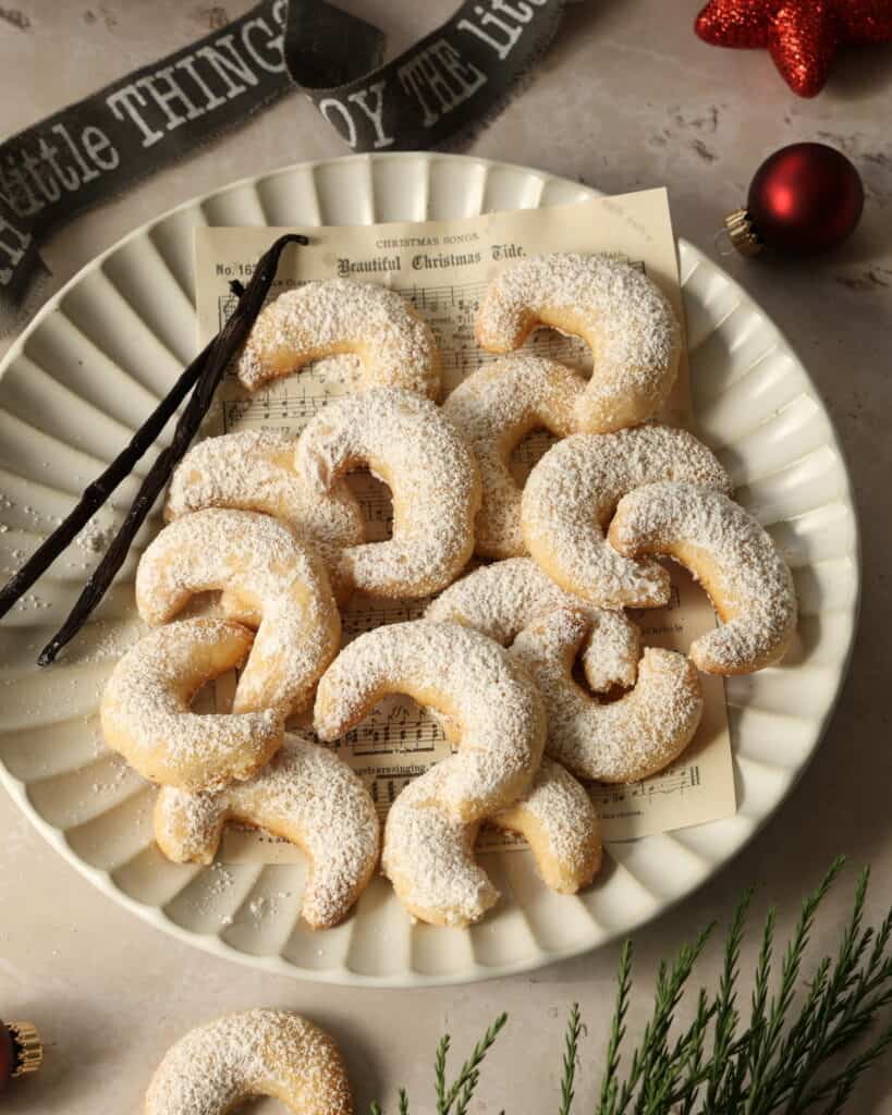 A white plate with vanilla crescent cookies and two vanilla pods.