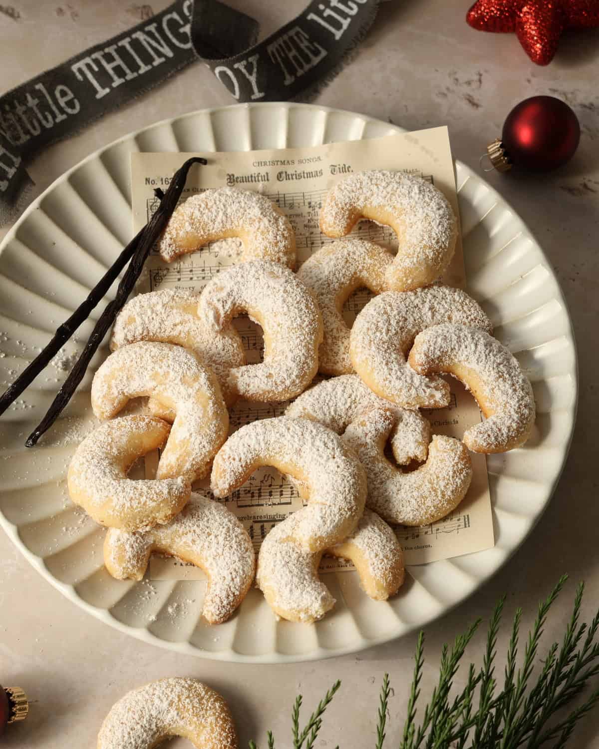 A white plate with vanilla crescent cookies and two vanilla pods.