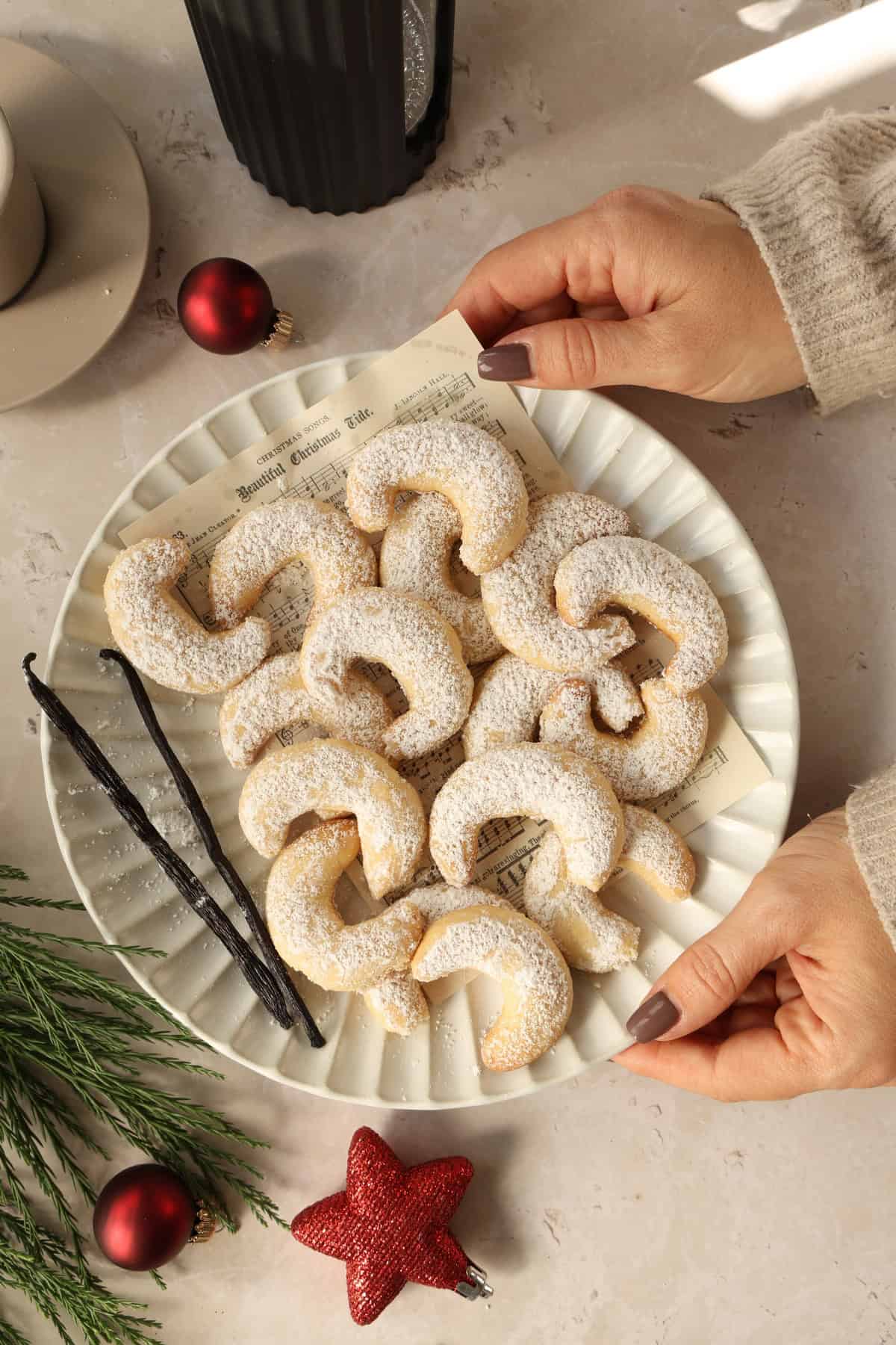 Two hands holding a plate of vanilla crescent cookies.
