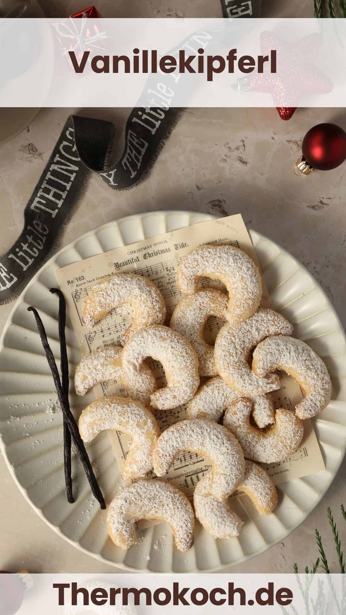 Ein weißer Teller mit Vanillekipferl und zwei Vanillestangen. Außen herum weihnachtliche Deko.