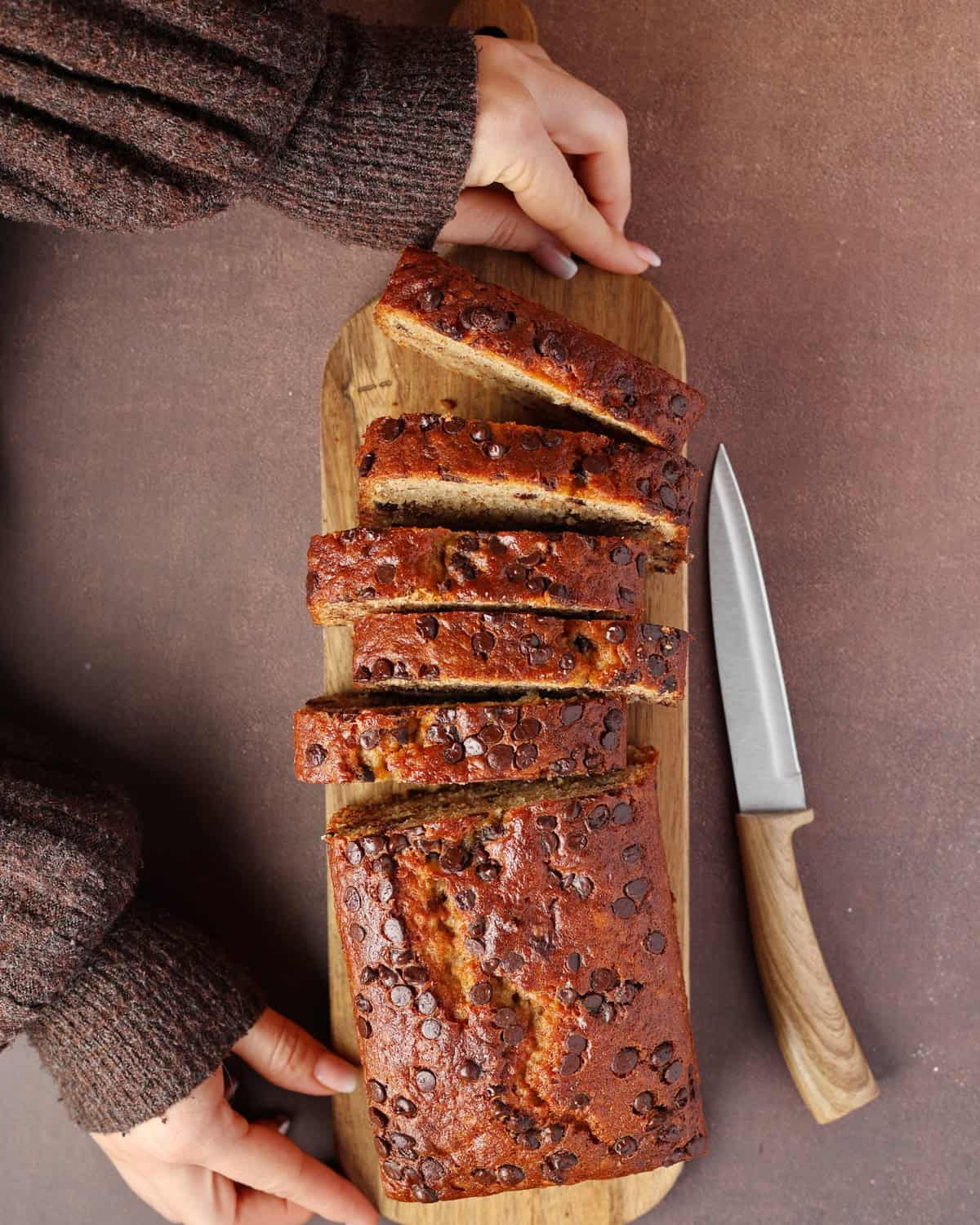 Two hands holding a sliced banana bread with chocolate chips.