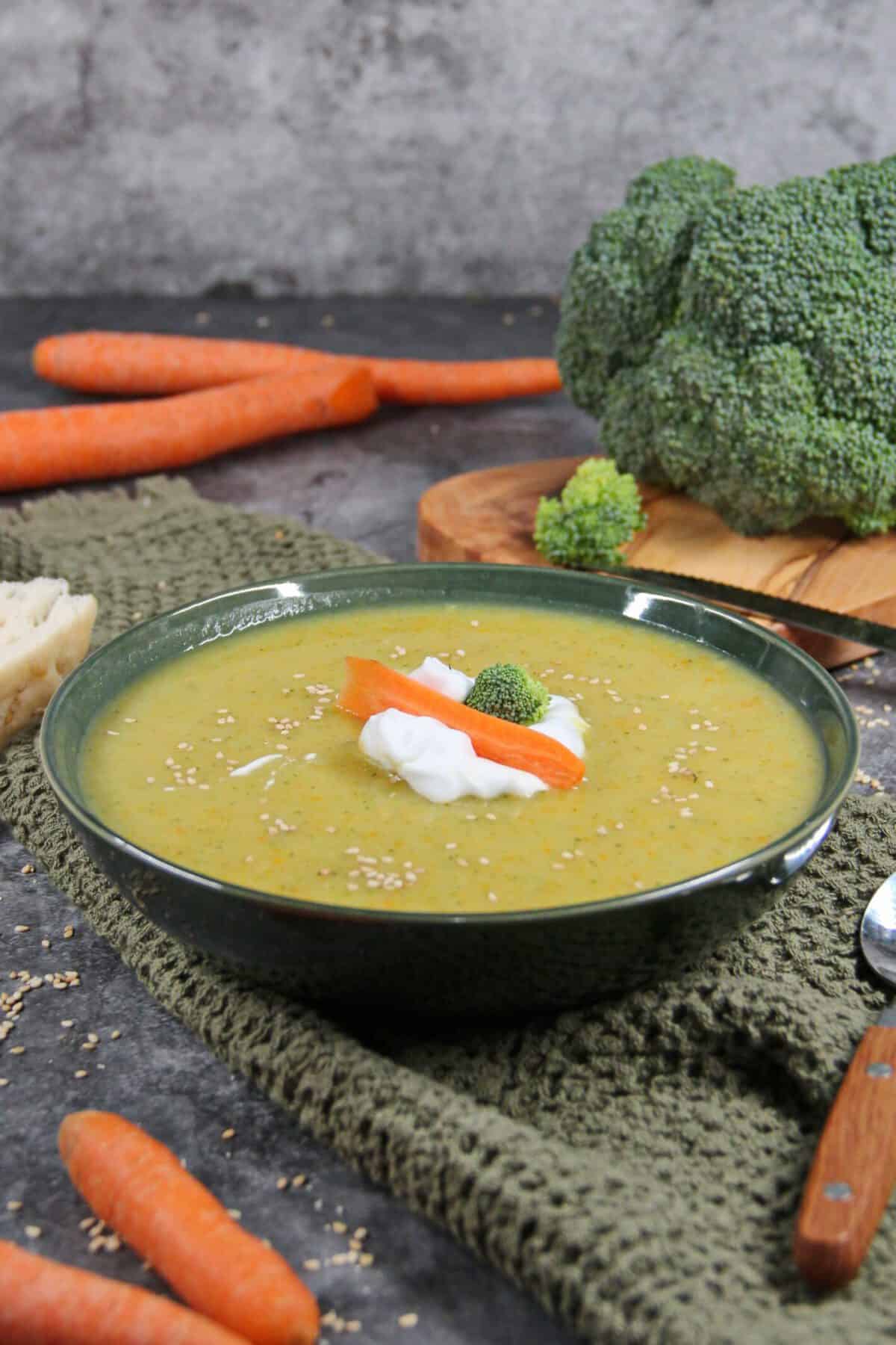 A dark soup bowl filled with creamy potato soup topped with sour cream and carrots.