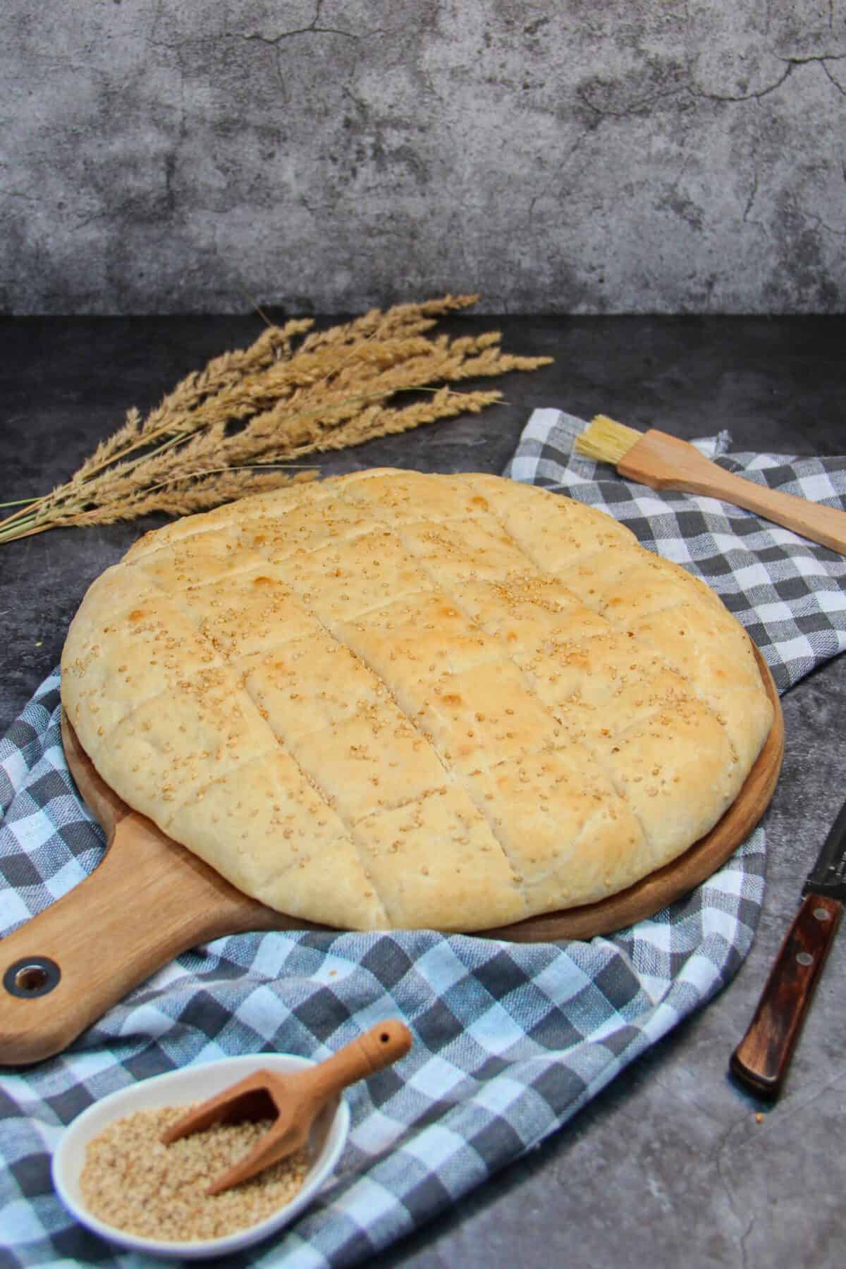 Freshly baked homemade flatbread topped with sesame seeds resting on a wooden board with a checkered cloth.