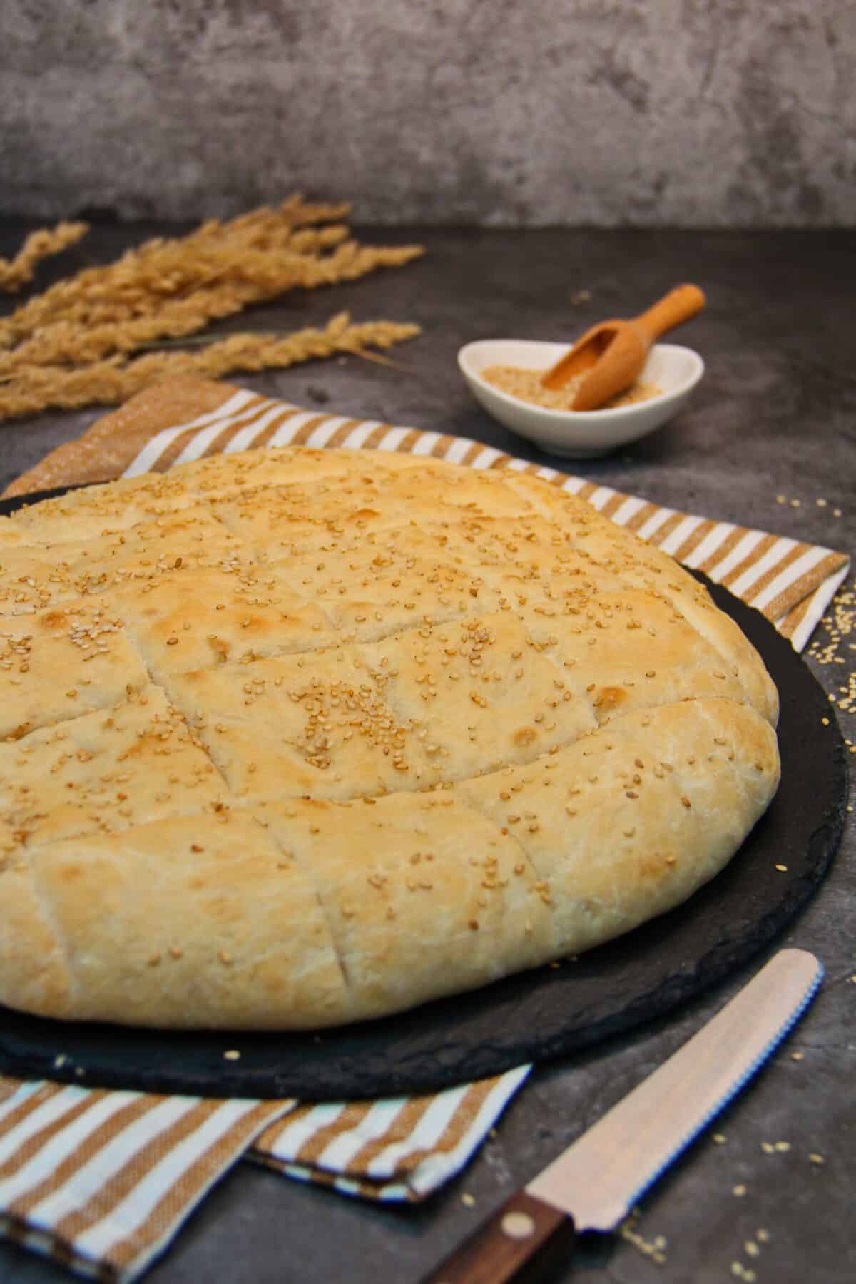 A golden-brown homemade sesame flatbread on a slate board next to a knife.