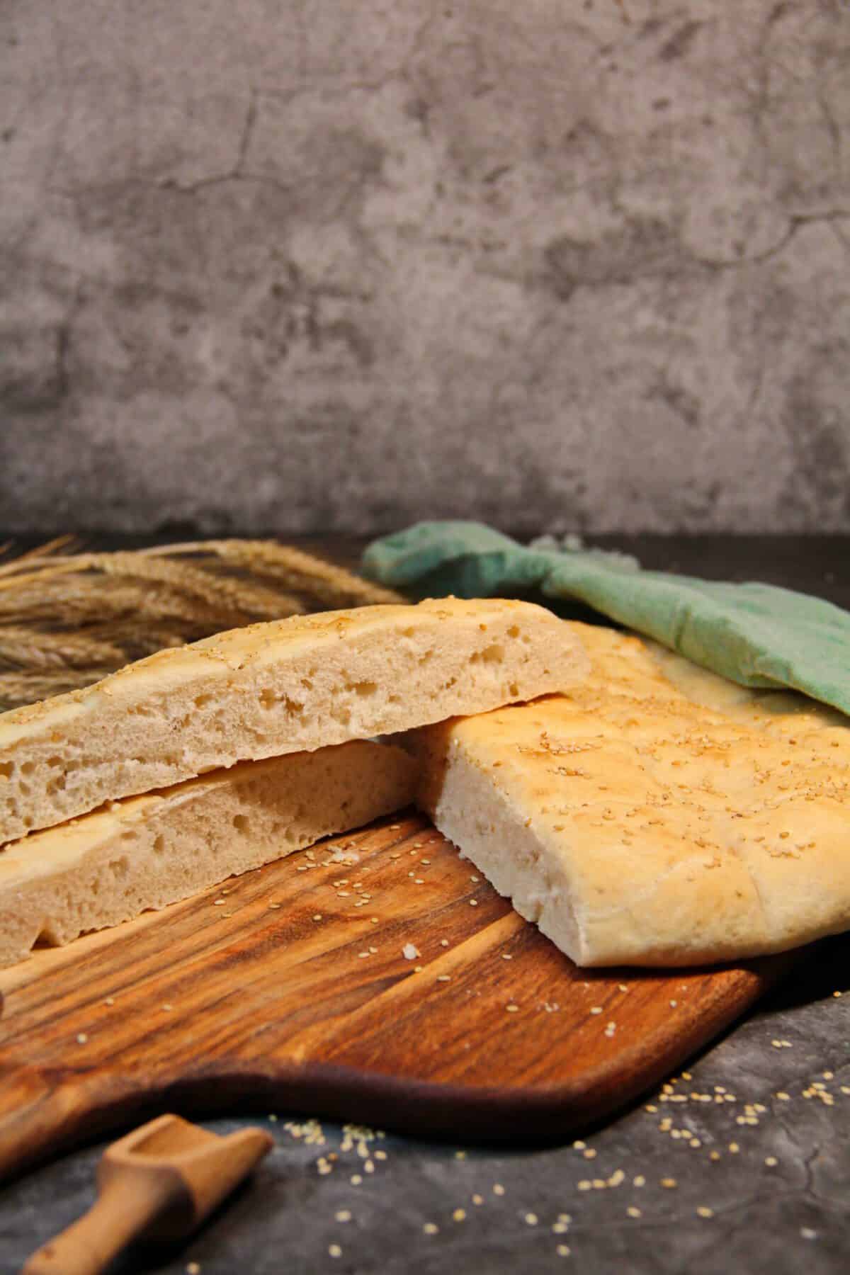Sliced homemade flatbread topped with sesame seeds on a wooden board, showing a soft, fluffy interior.