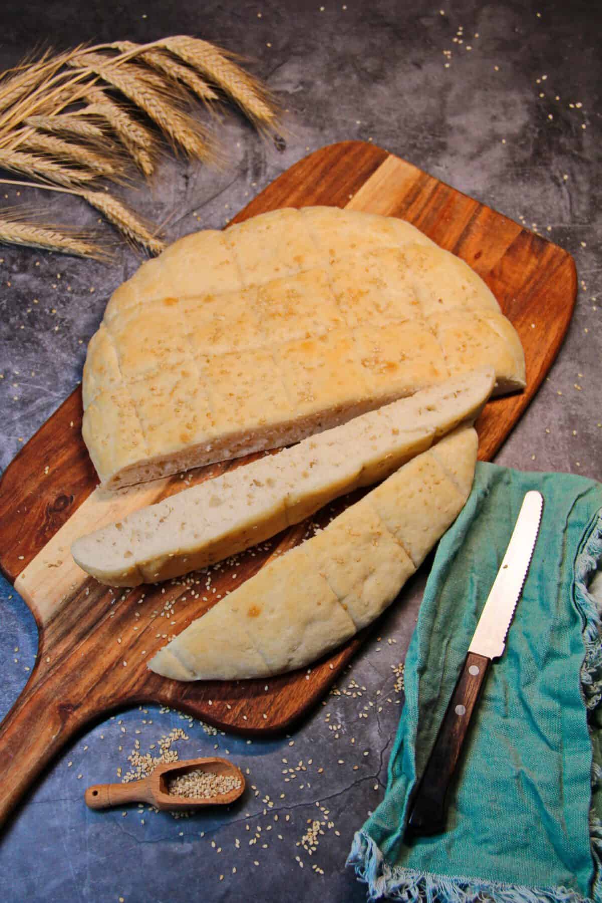 A sliced, freshly baked homemade flatbread topped with sesame seeds on a wooden cutting board.