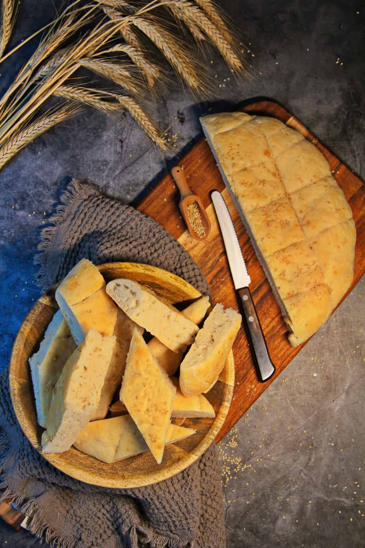Sliced homemade flatbread topped with sesame seeds, served on a wooden board and in a bowl.