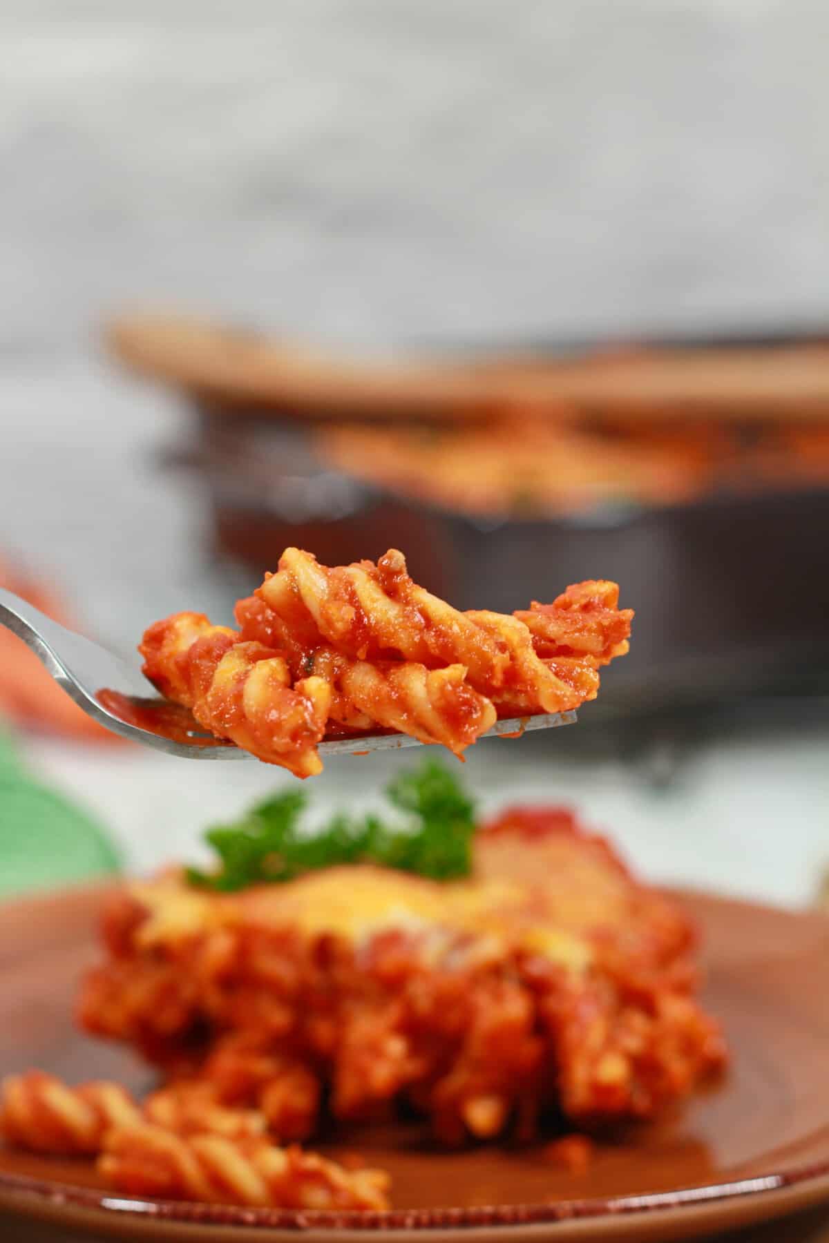 A bite of baked pasta on a fork with the casserole plate in the background.